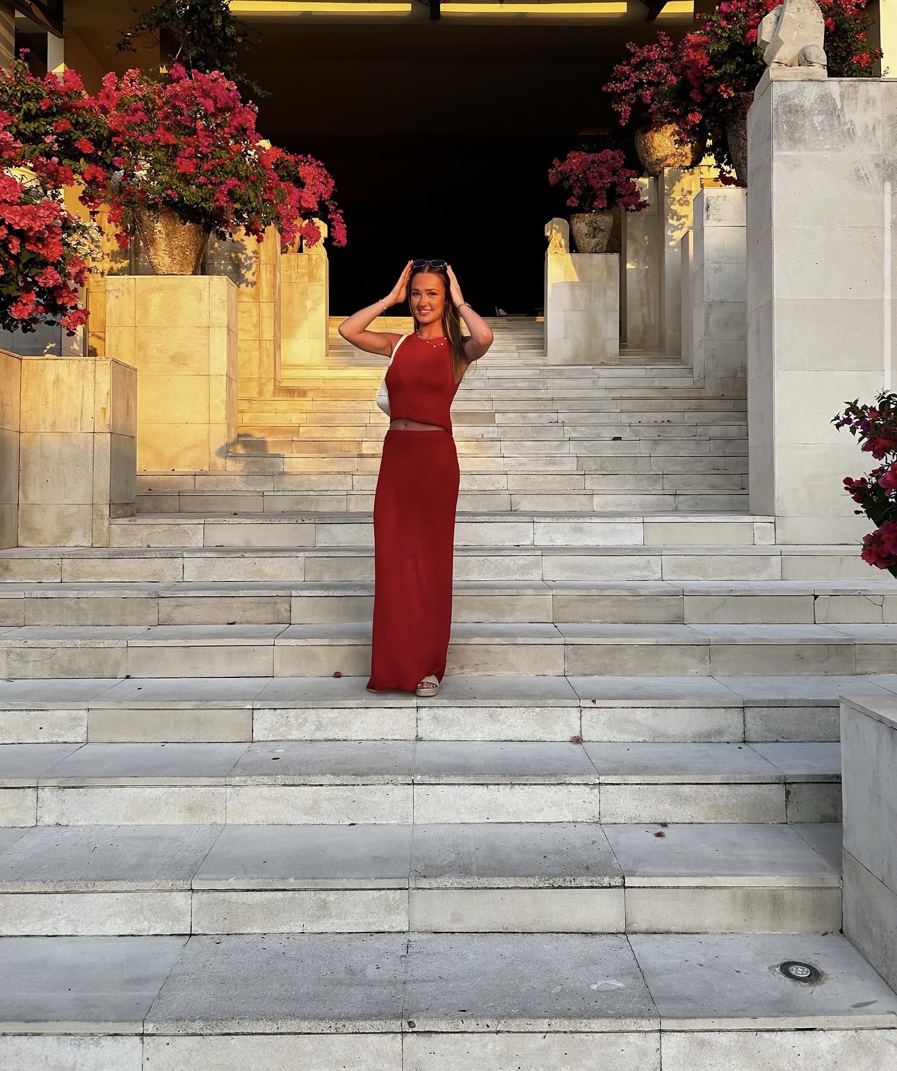 Skye in a long red dress on white stone steps lined with flowers